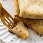 two crepes on a plate with recipe ingredients nearby and a fork taking a bite out of one.