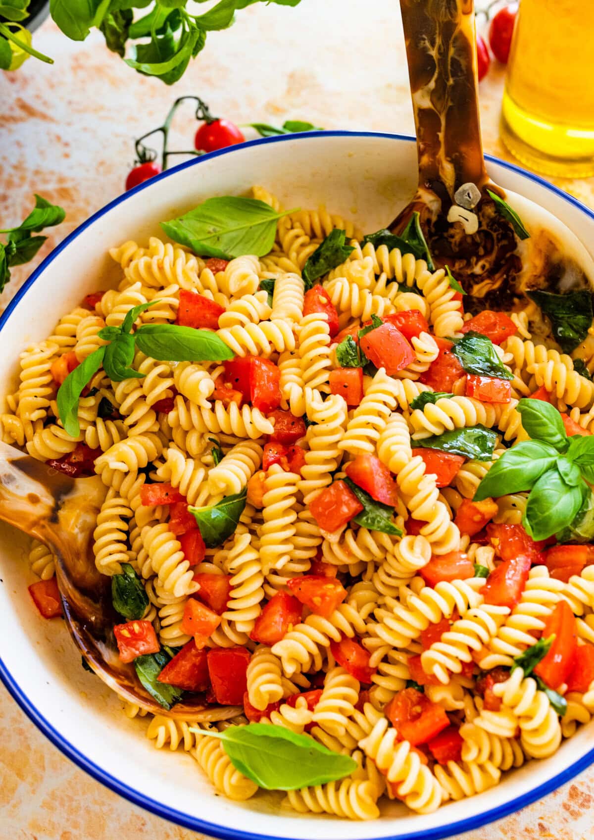 fresh tomato basil pasta on a blue and white serving bowl with serving spoon.