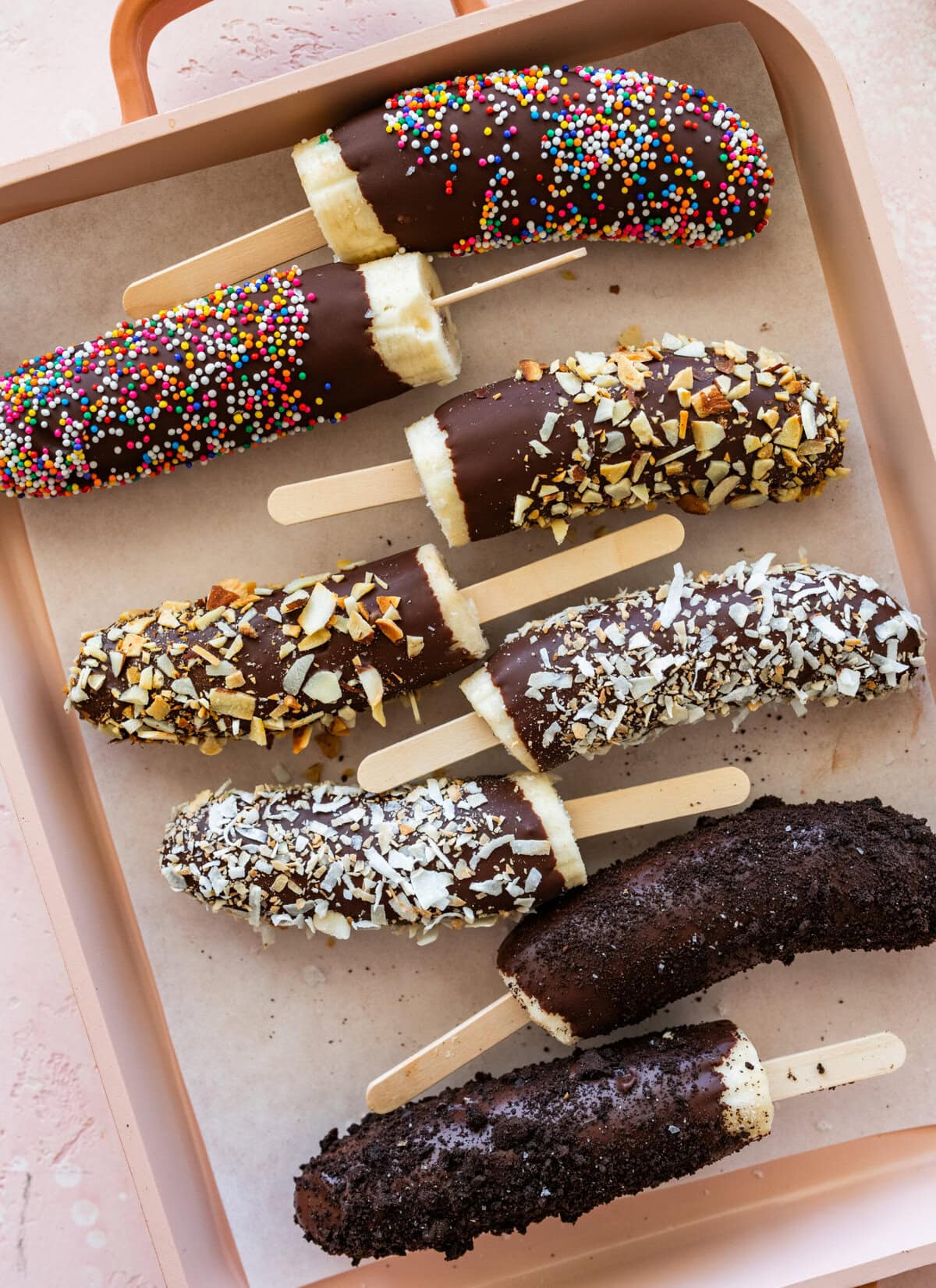 a few chocolate dipped bananas with toppings laid next to each other.