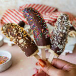 Three chocolate dipped bananas held over a tray of more.
