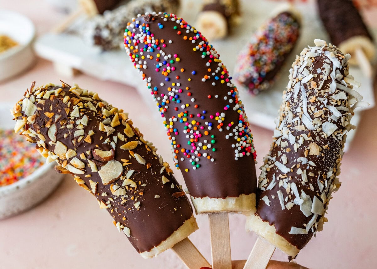Three chocolate dipped bananas held over a tray of more.