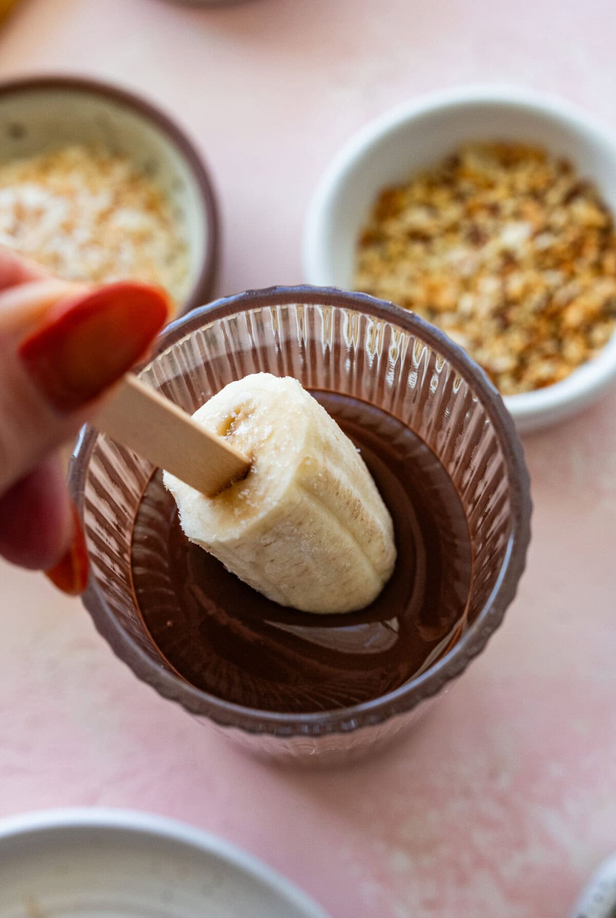 submersing a banana in a cup of melted chocolate until it reaches close to the stick.