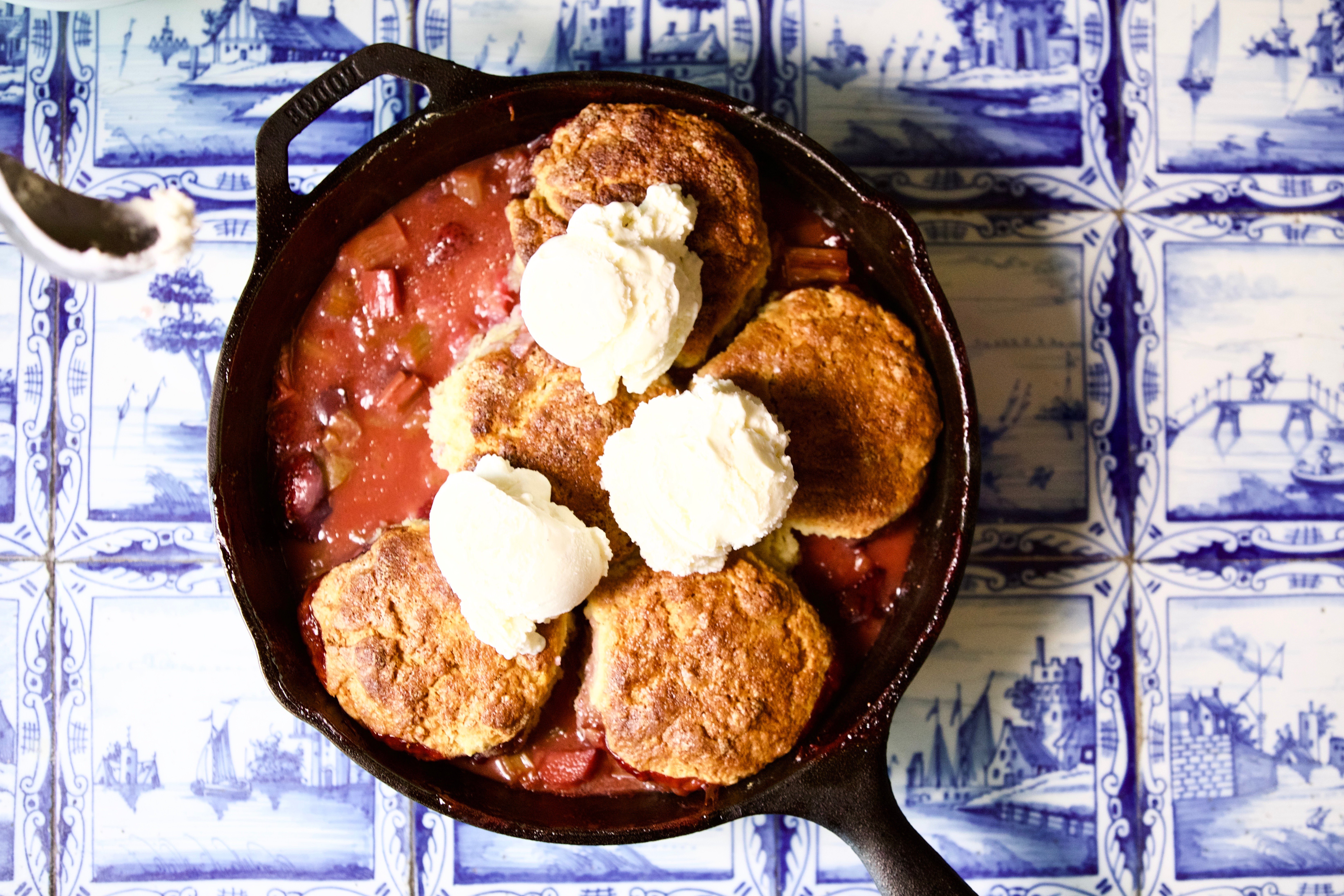 Rhubarb biscuit with ice cream in a skillet on a blue tiled background.