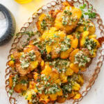 Smashed potatoes on a plate topped with the marinade and garnish, with more ingredients nearby.