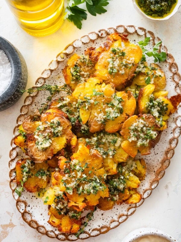 Smashed potatoes on a plate topped with the marinade and garnish, with more ingredients nearby.