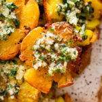 Smashed potatoes on a plate topped with the marinade and garnish, with more ingredients nearby.