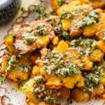 Smashed potatoes on a plate topped with the marinade and garnish, with more ingredients nearby.