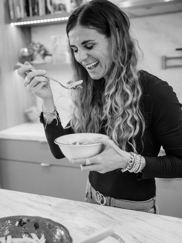 Black and white image of Elena holding a fork of food and smiling.
