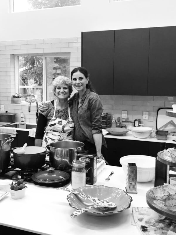 Black and white photo of two people in a full kitchen.