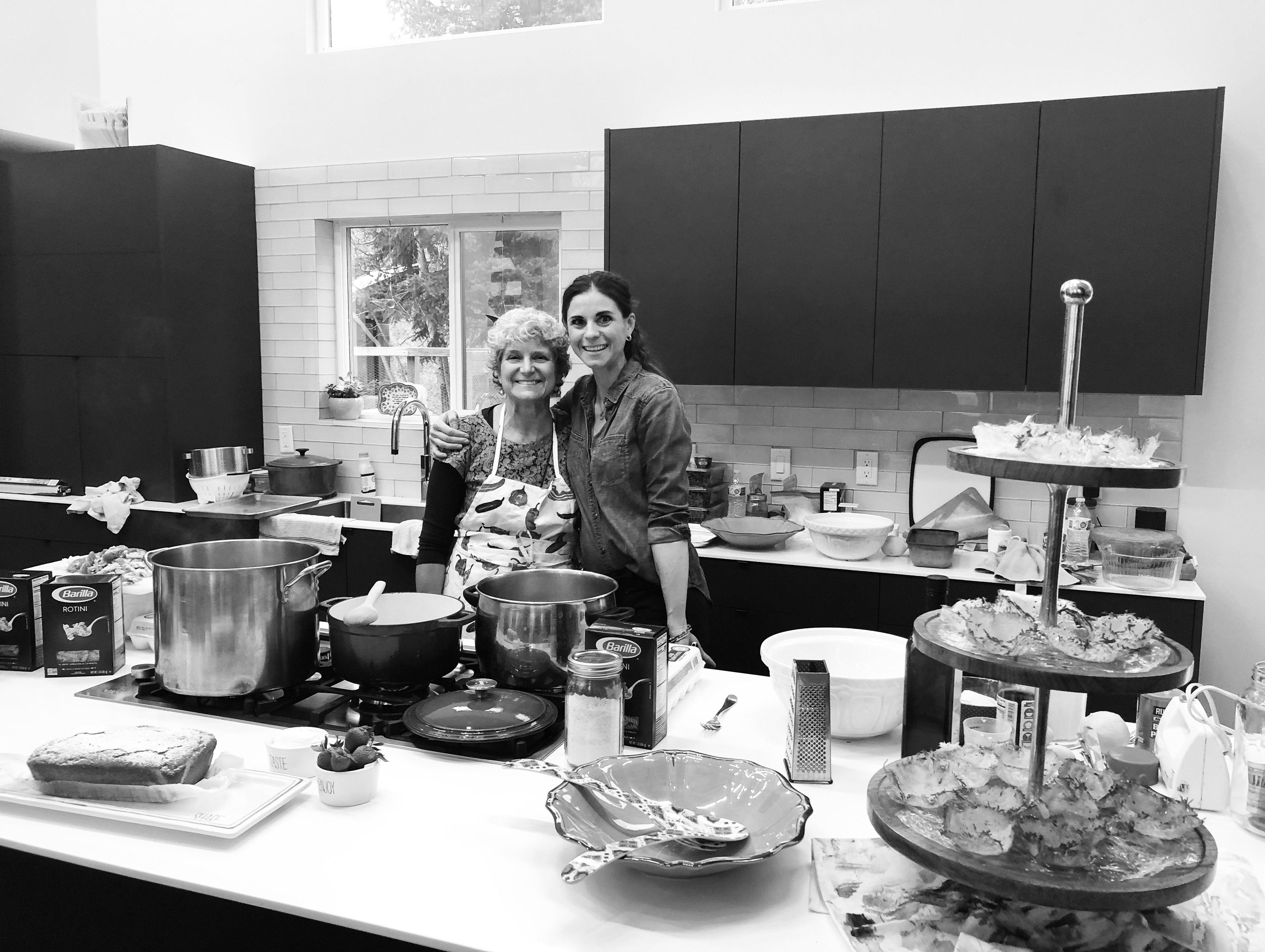 Elena and her mother hugging and smiling in a large kitchen with cooking supplies.