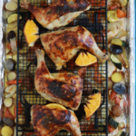 Orange chicken on a wire rack over potatoes and vegetables.