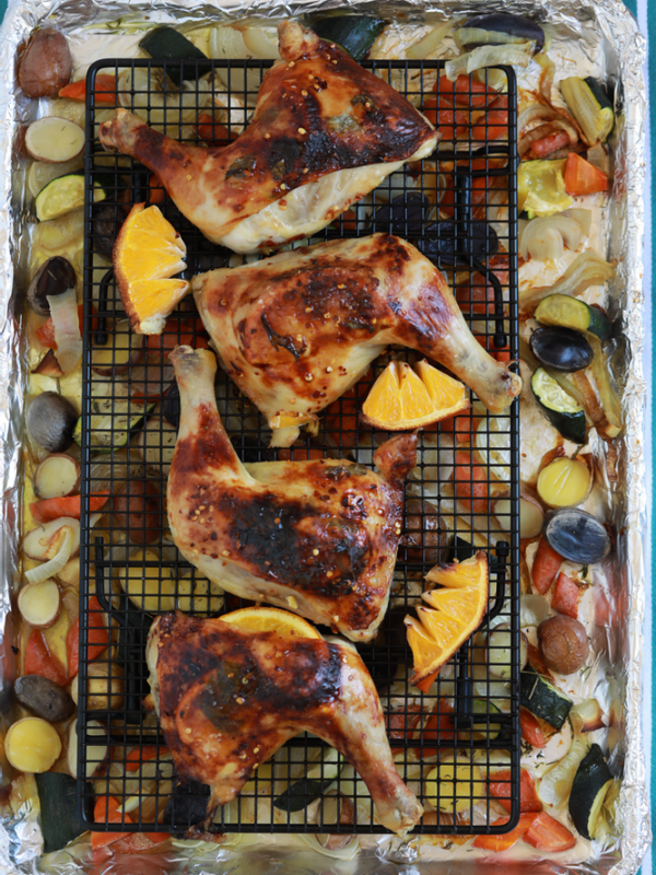Orange chicken on a wire rack over potatoes and vegetables.