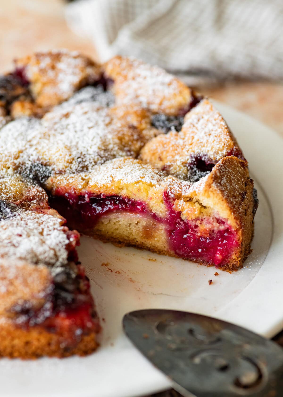 A plum torte on a dish with one slice removed.