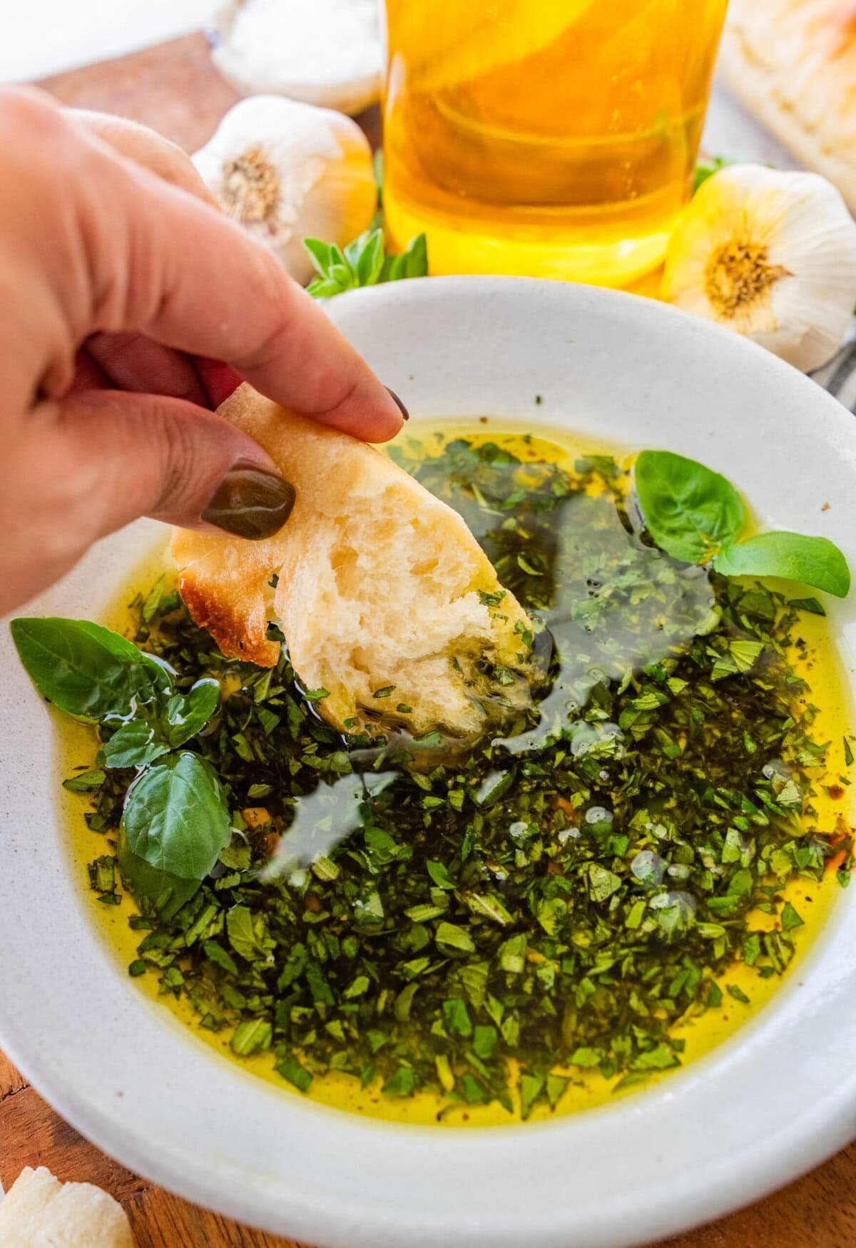 A hand dipping a slice of bread in an olive oil dip for bread.