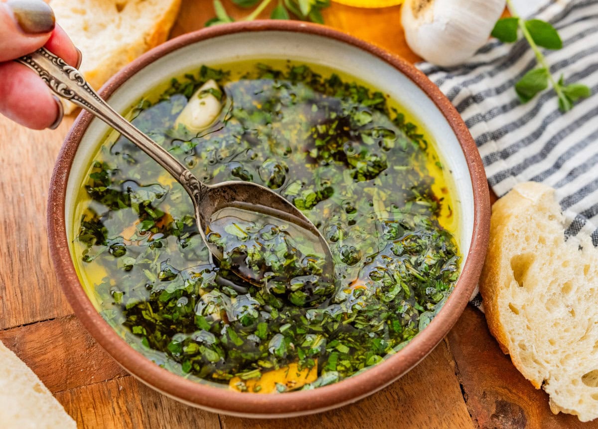 A bowl of bread dipping oil with a spoon lifting some up.