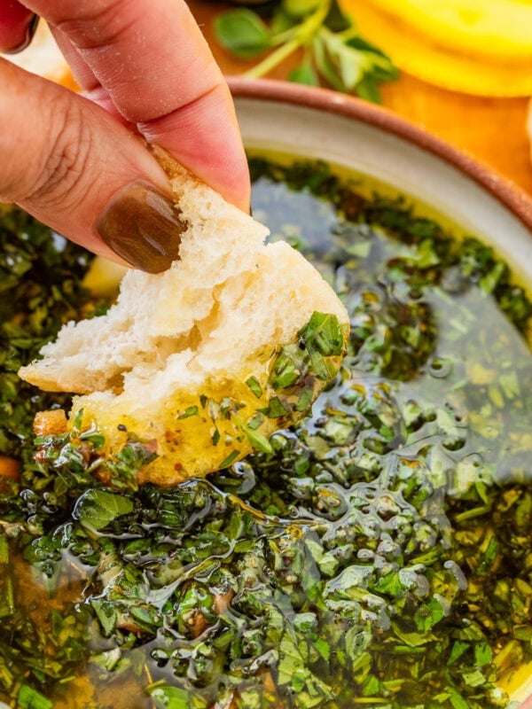 A hand dipping a piece of bread into a bowl of bread dipping oil.