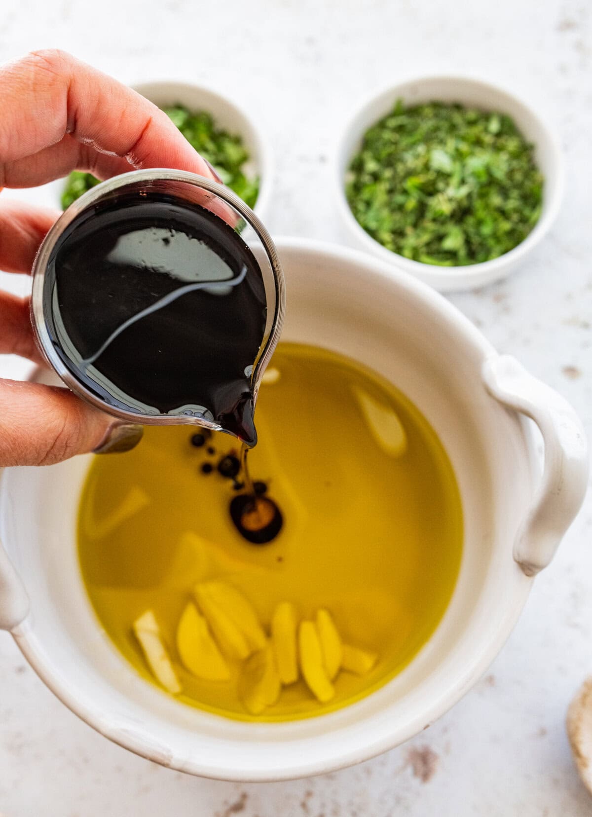 Adding balsamic vinegar to a bowl of olive oil and garlic.