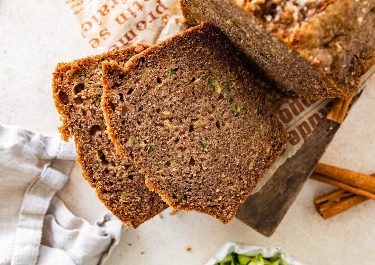 A loaf of zucchini bread with a few pieces cut off, and more ingredients nearby.