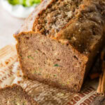 A loaf of zucchini bread with a few pieces cut off, and more ingredients nearby.