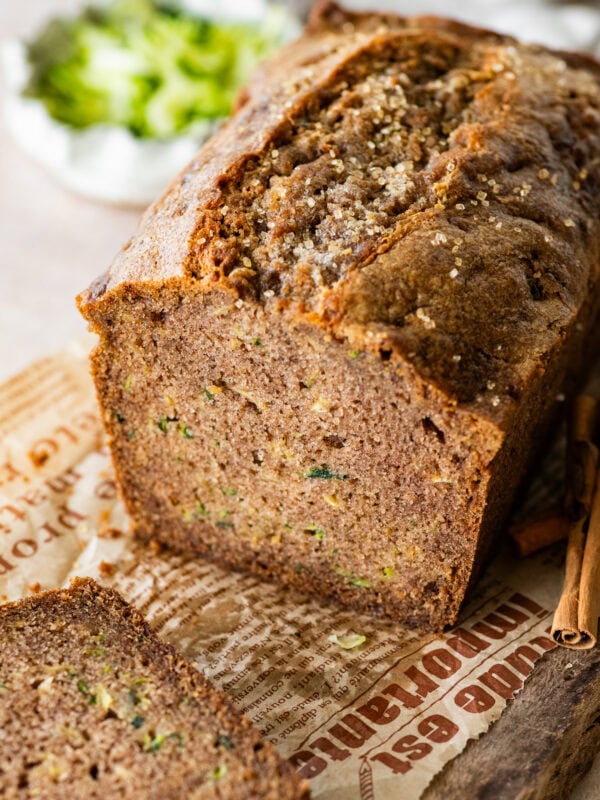 A loaf of zucchini bread with a few pieces cut off, and more ingredients nearby.