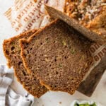 A loaf of zucchini bread with a few pieces cut off, and more ingredients nearby.