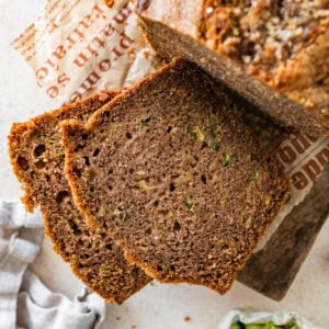 A loaf of zucchini bread with a few pieces cut off, and more ingredients nearby.