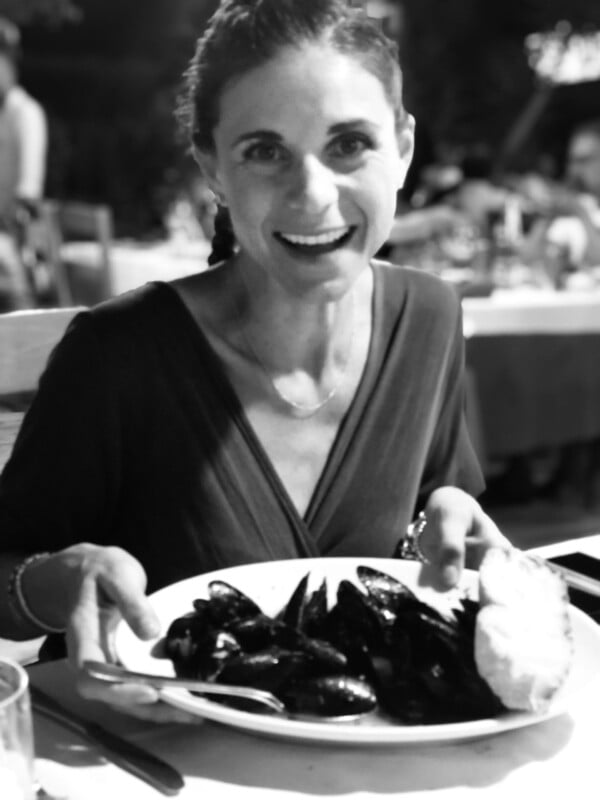 Black and white photo of a smiling woman holding a plate of food.