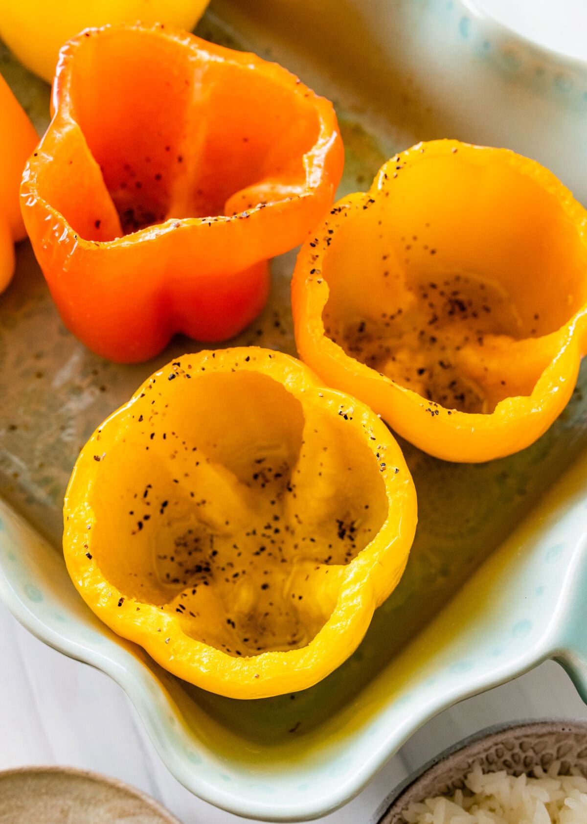 Hollowed out bell peppers in a white casserole dish and partially baked.