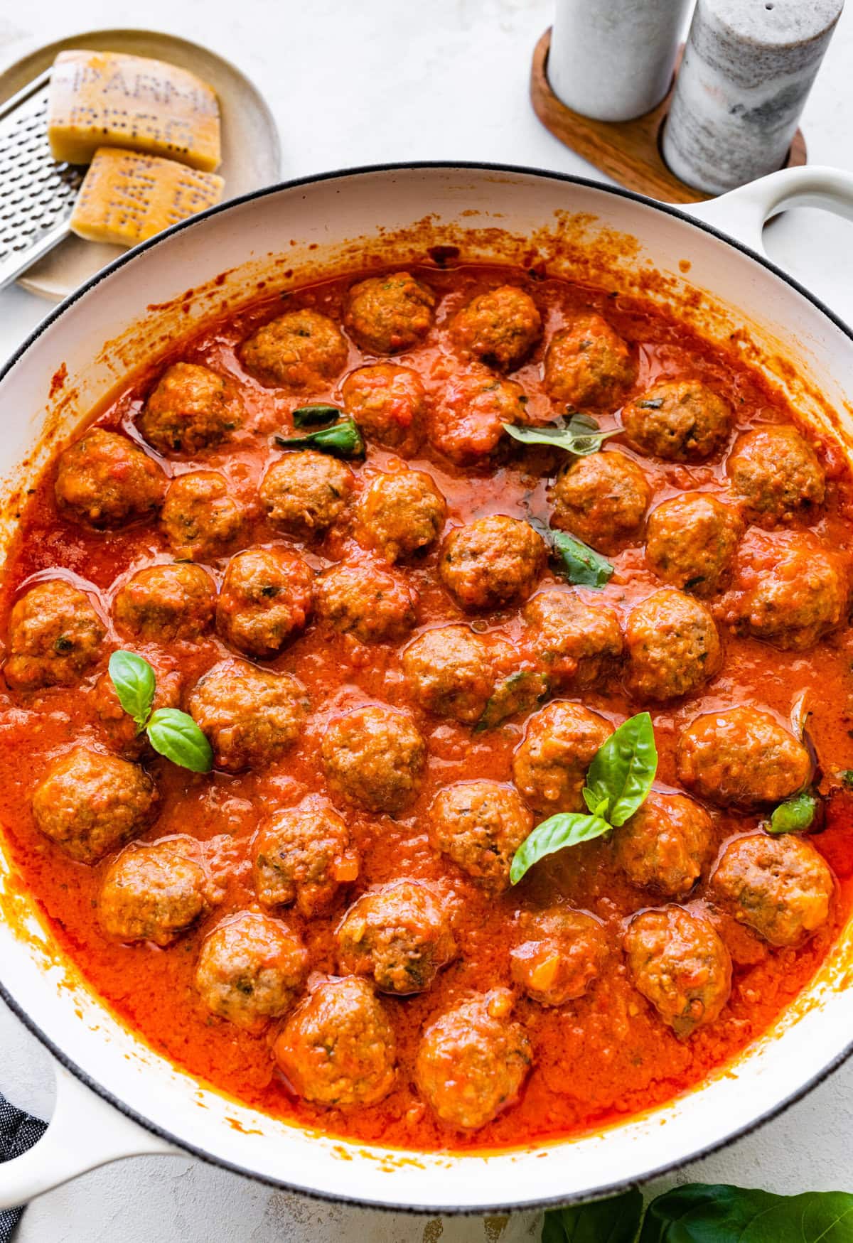 cooked meatballs in pan with sauce and basil on top.