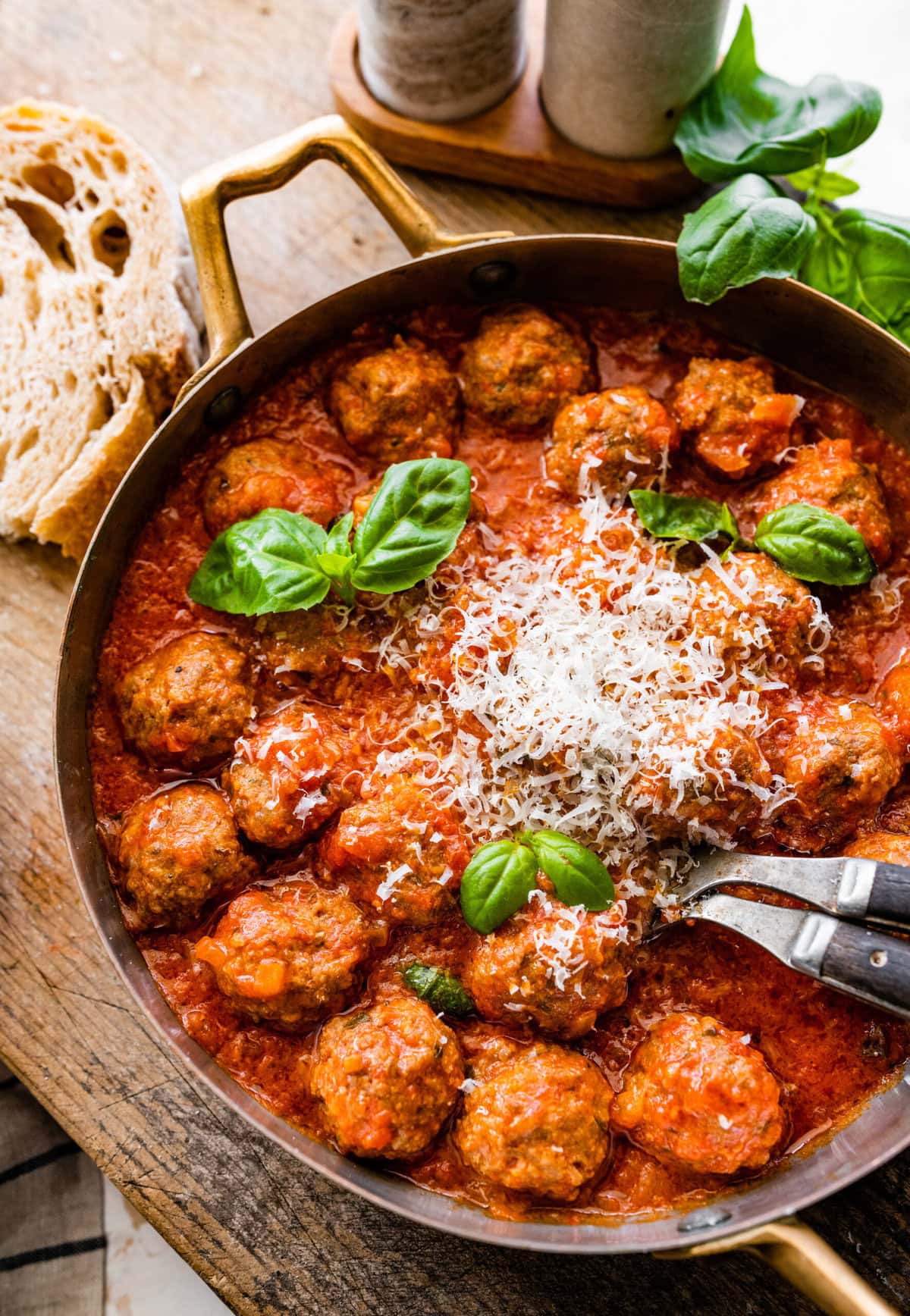 cooked meatballs in a round serving platter with serving utensils and basil on the side. Close up of the meatballs in the sauce.