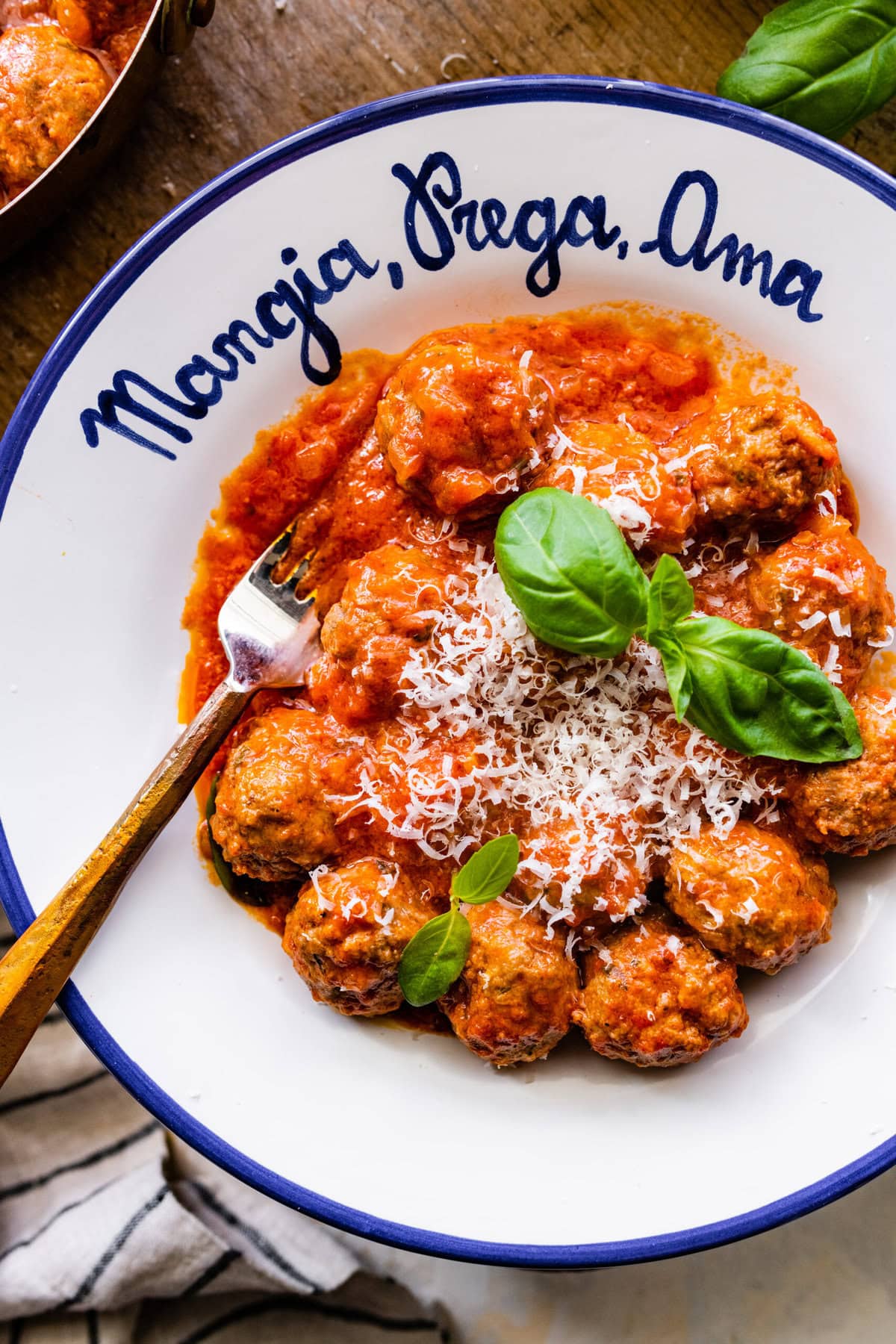 white Italian style bowl with the prepared meatballs in sauce with parmigiano cheese on top and fresh basil leaves.