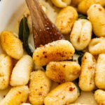 Gnocchi with brown butter sage sauce in a skillet with a wooden spoon resting inside.