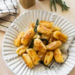 A plate of brown butter sage gnocchi with a fork resting on it.
