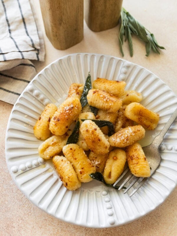 A plate of brown butter sage gnocchi with a fork resting on it.