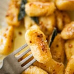 A fork holding one gnocchi over a plate of more brown butter sage gnocchi.