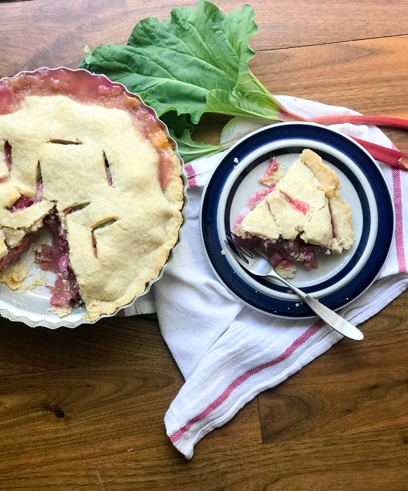  Rhubarb Pie in a pie tin with one slice on a plate.