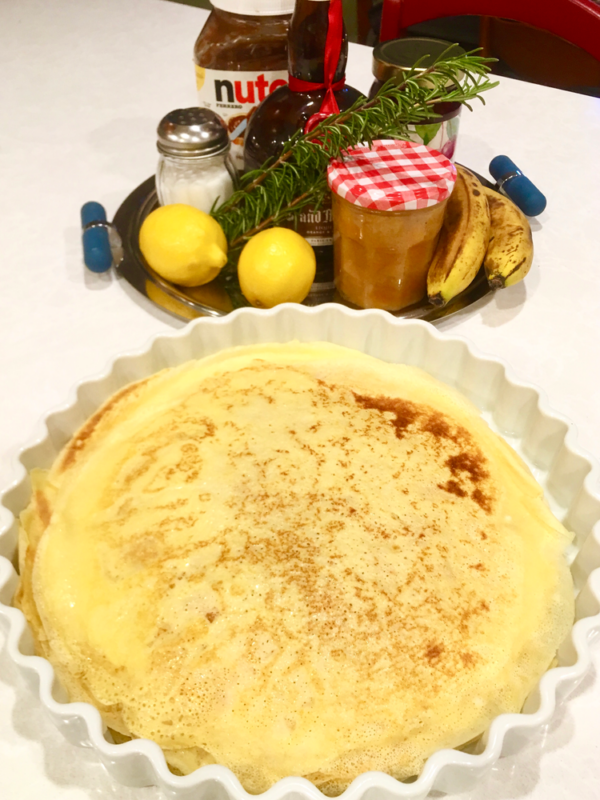 French crepes in a fluted bowl with a plate of possible toppings.
