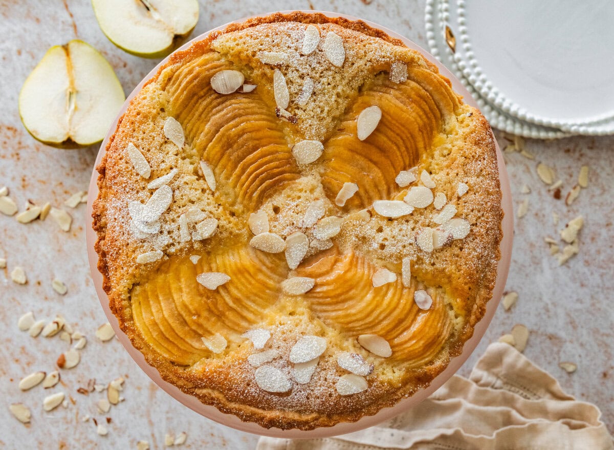 Pear frangipane tart with nuts as garnish and more ingredients and serving ware nearby.