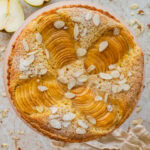 Pear frangipane tart with nuts as garnish and more ingredients and serving ware nearby.