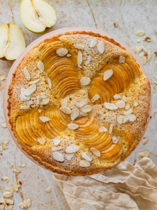 Pear frangipane tart with nuts as garnish and more ingredients and serving ware nearby.