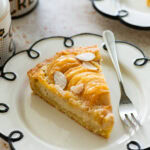 A slice of pear frangipane tart on a plate with a fork.