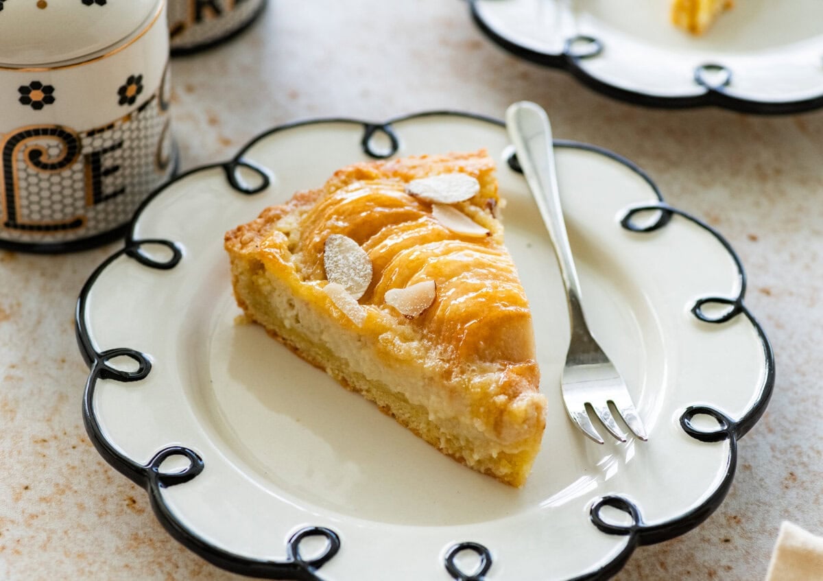 A slice of pear frangipane tart on a plate with a fork.
