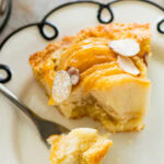A slice of pear frangipane tart on a plate with a fork holding up one bite.