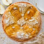 Pear frangipane tart with nuts as garnish and more ingredients and serving ware nearby.