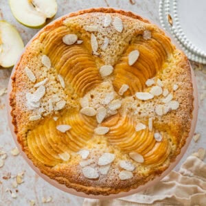 Pear frangipane tart with nuts as garnish and more ingredients and serving ware nearby.