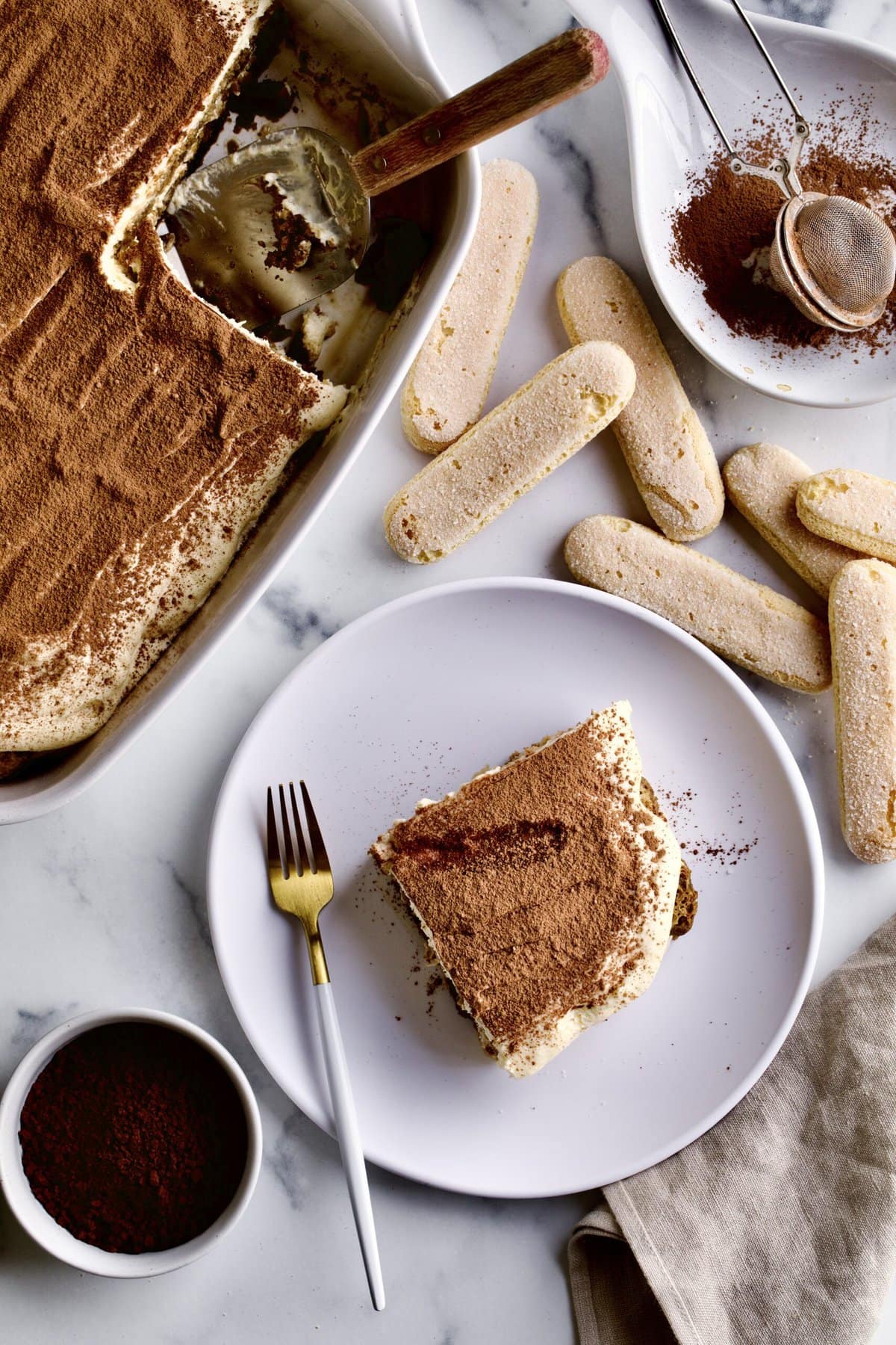 slice of tiramisu on a plate with ladyfinger cookies in the background.