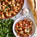 Trottole Pasta Recipe with Tomato Sauce and Shrimp in red enamel pan with bowl of pasta on side.