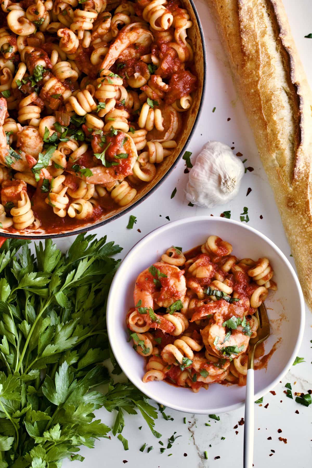 Trottole Pasta Recipe with Tomato Sauce and Shrimp in red enamel pan with bowl of pasta on side.