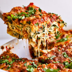 Spinach lasagna slice from pan with cheese pulling.