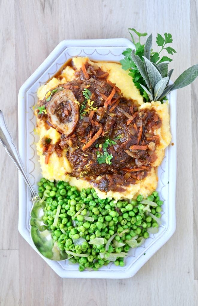Maremma-style lamb osso buco on a plate with green peas and polenta 
